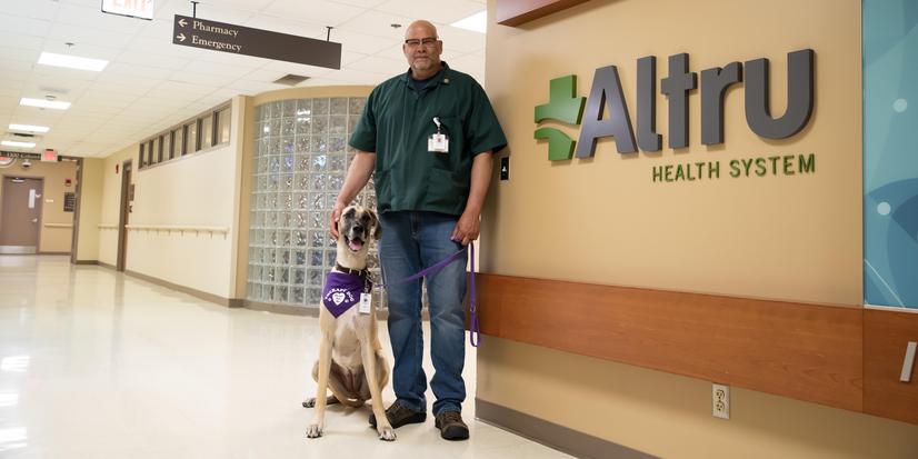 Eric standing in a hall with Sophie, Altru's therapy dog.