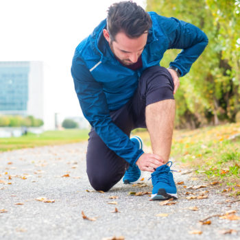 man bending touching his ankle while on a run