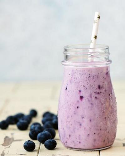 A blueberry smoothie in a jar surrounded by blueberries.