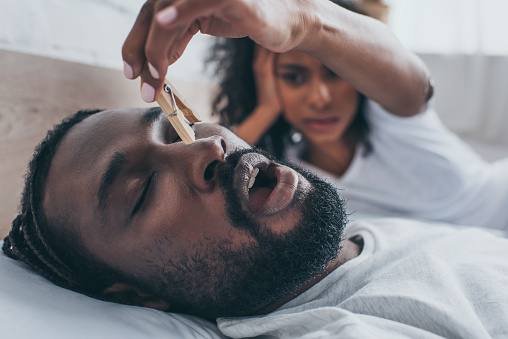 A person placing a clothespin on a person's nose to stop them from snoring.