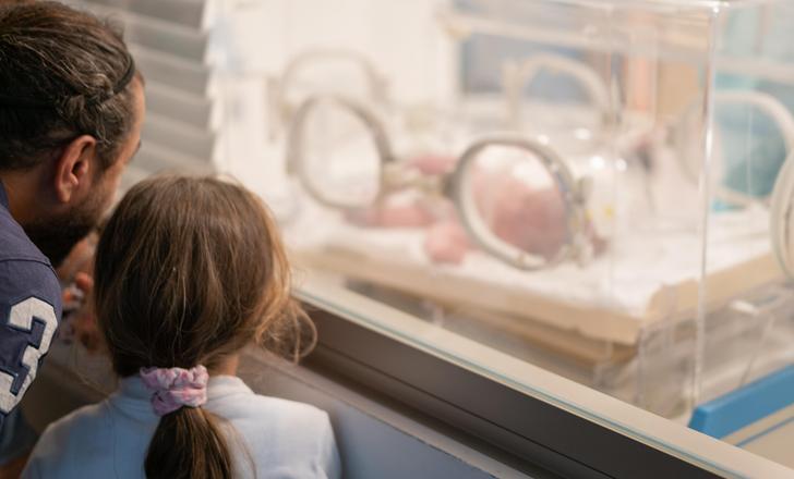 Hospital visitors looking at a baby in the NICU through a window.