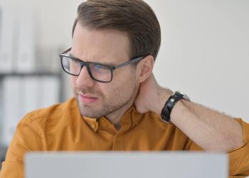 A man grabbing his neck in front of a computer.