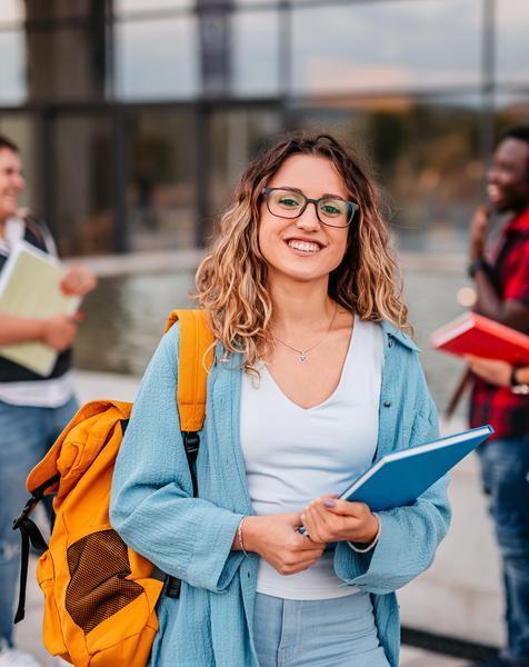 A student holding books outside of a school.