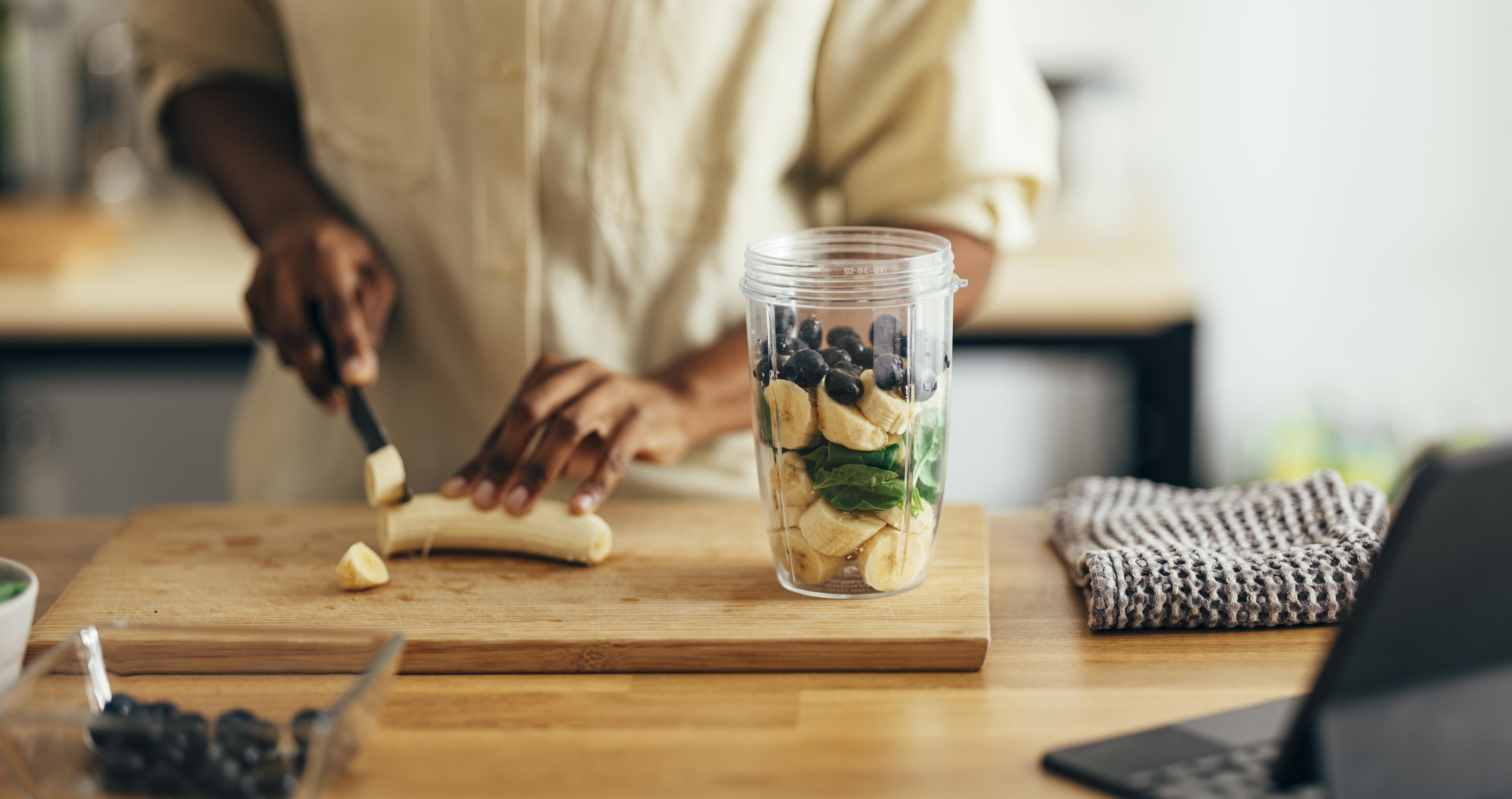 Person cutting up a banana to put in a smoothie.