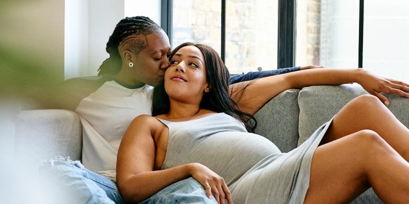black LGBT couple lays on sofa-pregnant woman touches the other woman's leg