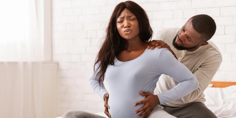 black pregnant woman touches stomach while man touches her shoulders.