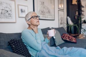 older woman holding throat and coffee in other hand