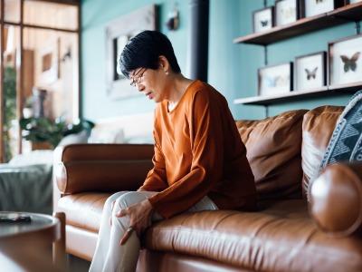 An older woman sitting on a couch holding her knee due to knee pain.