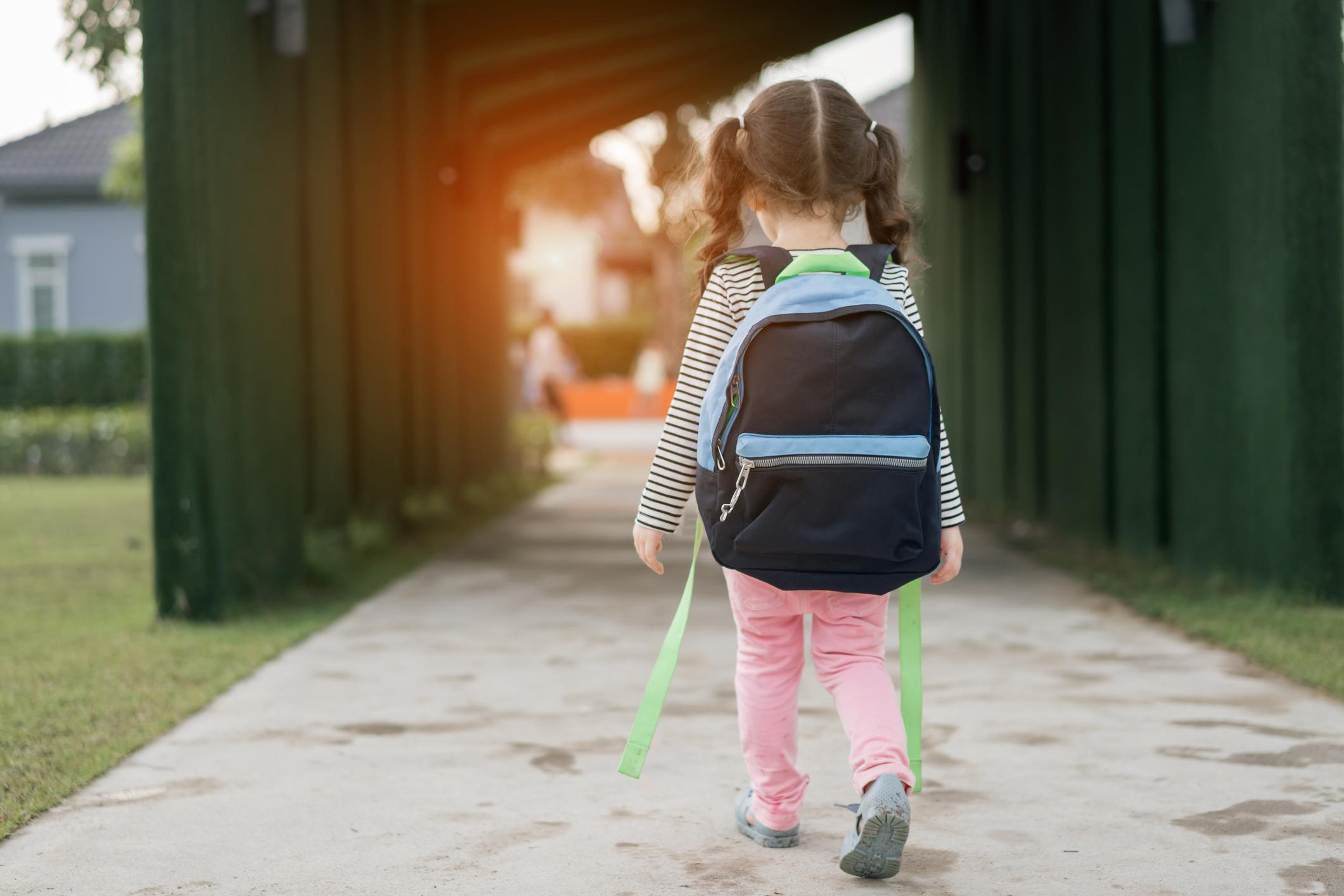 Child with a backpack walking on the sidewalk.